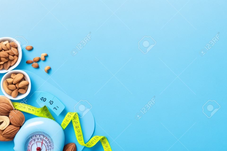 weight loss concept. Top view photo of scales fruits vegetables nuts almonds cashew and tape measure on isolated pastel blue background with empty space