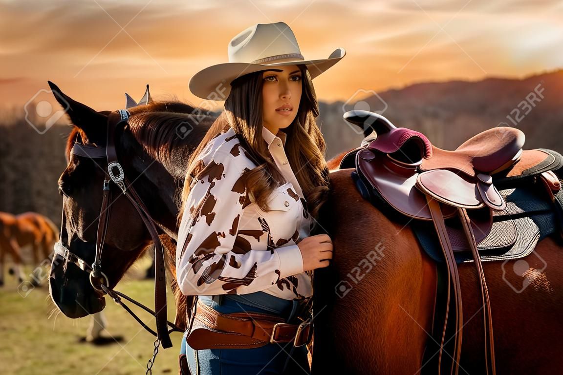 A beautiful brunette cowgirl poses with her horse before riding in the country