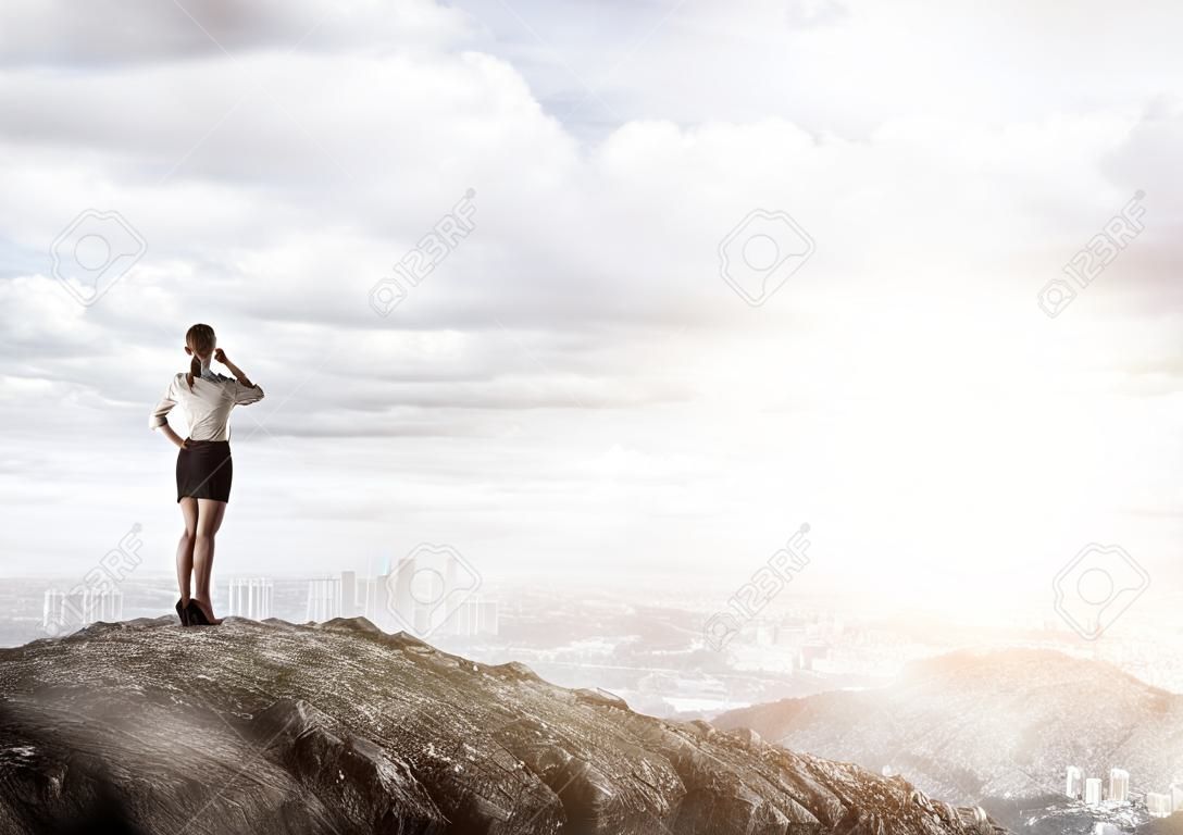 Businesswoman standing with back on top of hill and viewing modern city