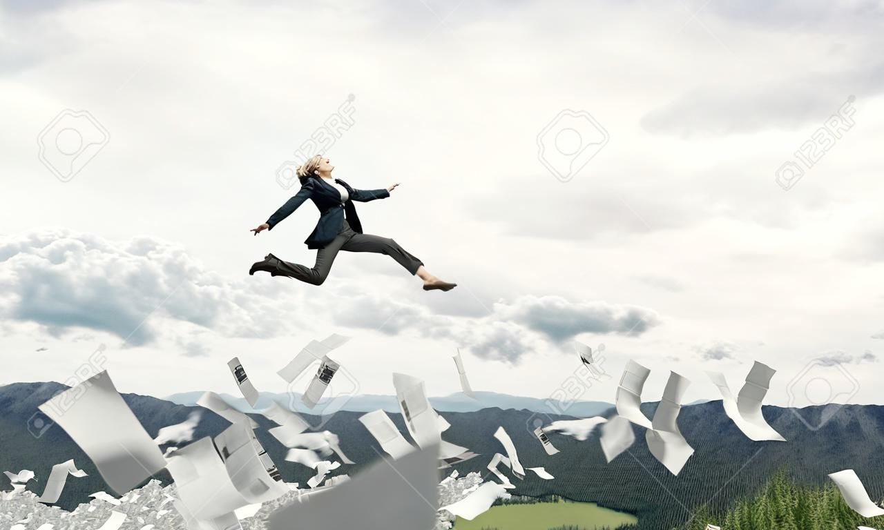 Attractive business woman in suit jumping in the air among flying papers as symbol of active life position. Skyscape and nature view on background. 3D rendering.