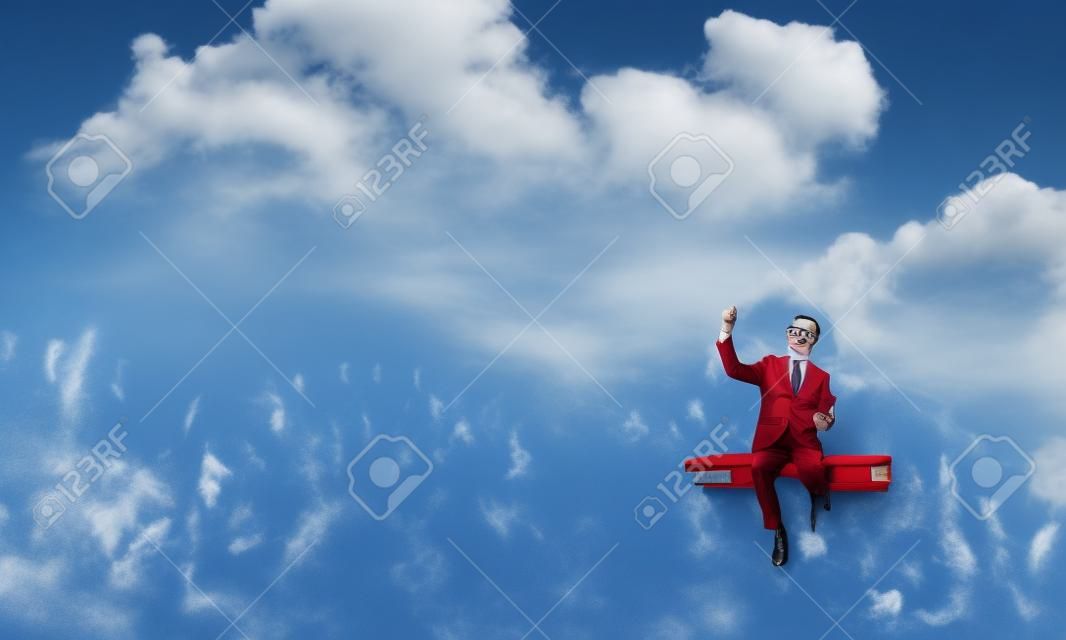 Zabawny mężczyzna w czerwonych okularach i garniturze siedzi na książce w błękitne niebo