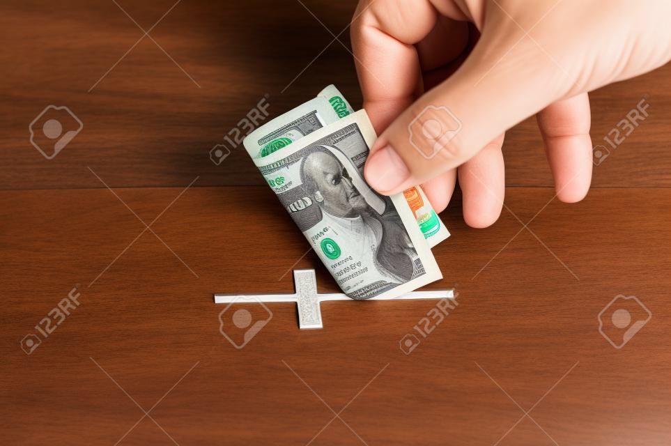 Man puts donation in his hand with dollar in slot in the form of Christian cross