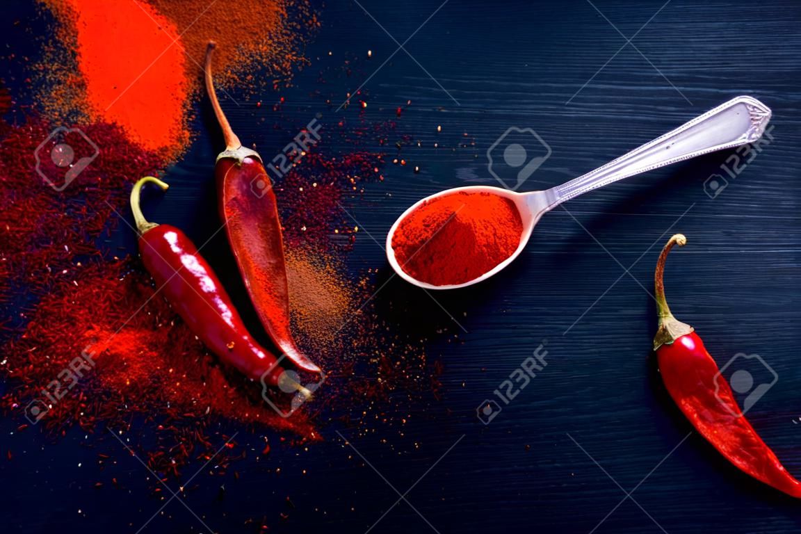 Rote Chiliflocken und Chilipulver platzen auf schwarzem Hintergrund
