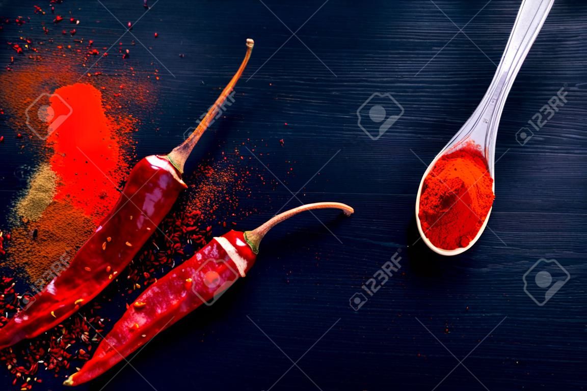 Rote Chiliflocken und Chilipulver platzen auf schwarzem Hintergrund