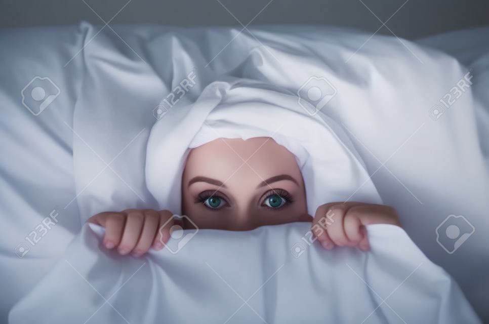 害怕的年輕女子躺在床上，躲在床單下