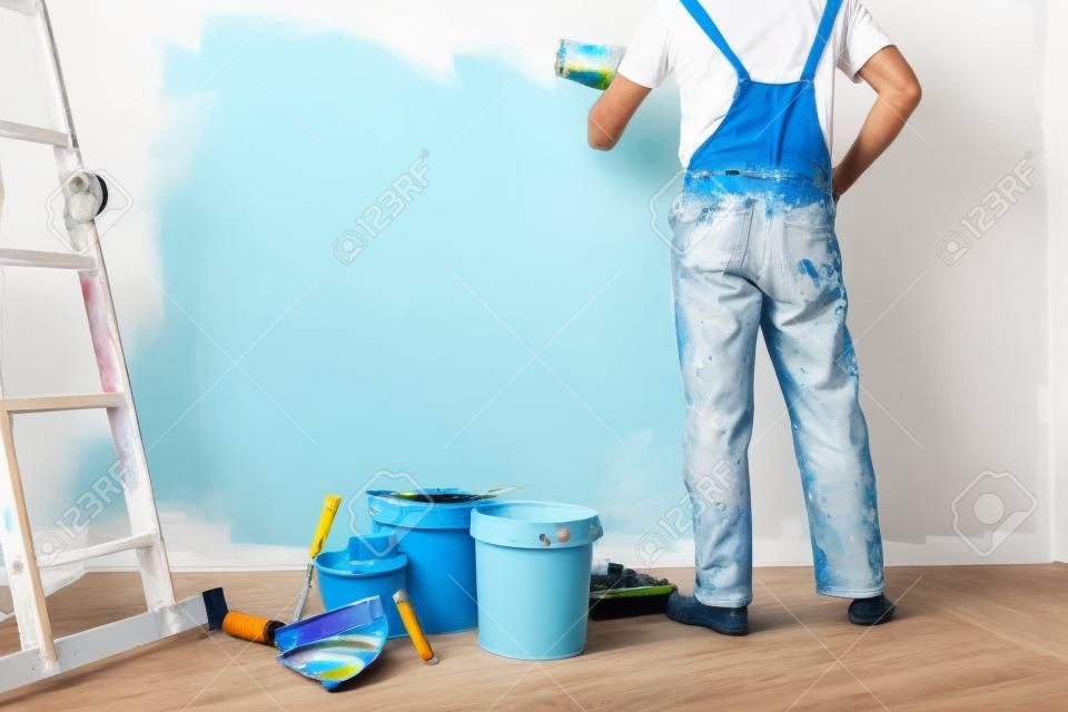 un hombre pinta una pared blanca con un rodillo. Reparación del interior. Joven decorador pintando una pared en la habitación vacía, creador de conceptos o pintor en casco con rodillo de pintura sobre la habitación vacía.