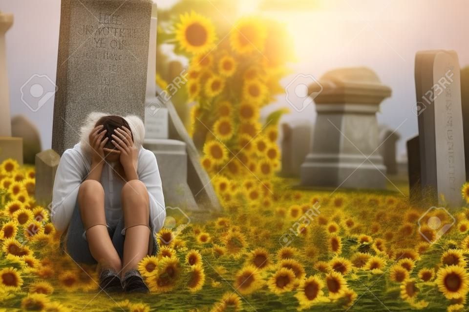 Piangere solitario giovane donna in lutto con girasoli di fronte a una lapide in un cimitero