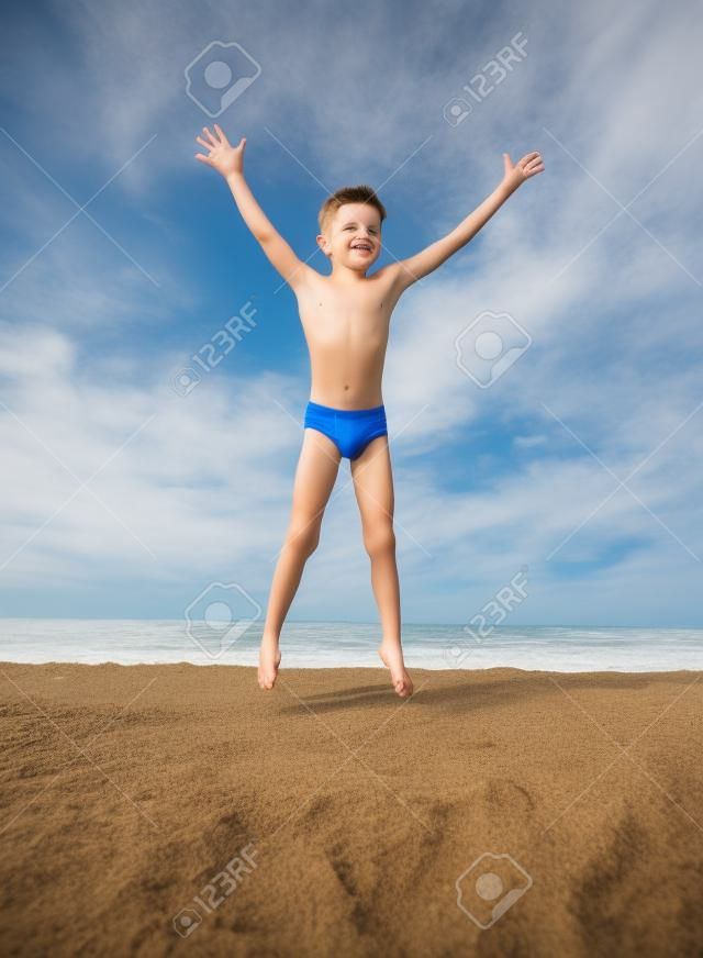 The boy jumps up on the sandy beach near the sea