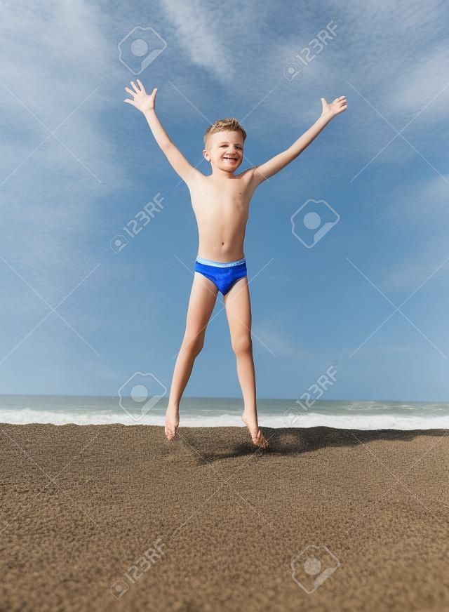 The boy jumps up on the sandy beach near the sea
