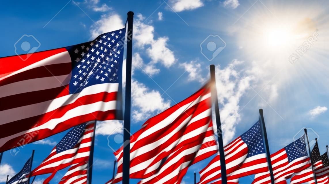 American flags flying in the wind against a blue sky with sun rays