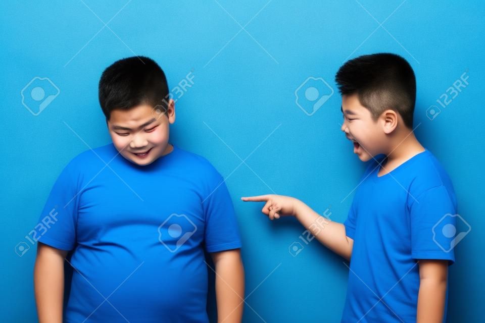 Asian boy bullying mocking other boy, fat boy get bullied at school, against blue background