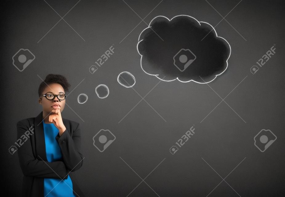 South African oder African American schwarze Frau Lehrer oder Schüler mit ihrer Hand auf ihrem Kinn, während Hintergrund gegen eine Kreidetafel stehen Wolke Gedanken oder Blase Denken innen