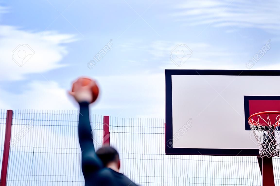 Homem atraente jogando basquete na quadra de basquete. O homem está fora de foco e em primeiro plano, fundo está no foco. Treinamento ao ar livre