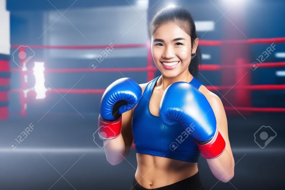 Boxer woman. Young Asian Boxing fitness woman smiling happy wearing blue boxing gloves with Boxing Stadium in background. Portrait of sporty fit for healthy lifestyle Asian model of boxing gym concept.