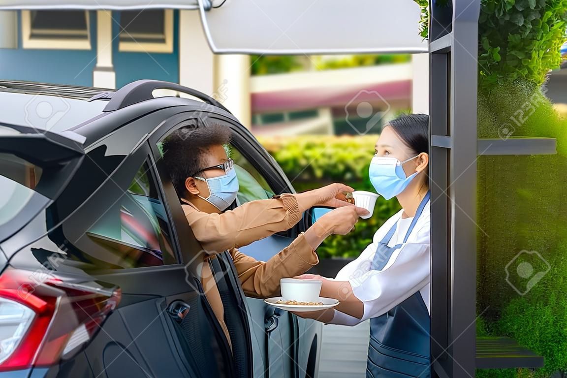 Uomo asiatico in maschera protettiva che prende cibo e caffè con cameriera donna che indossa maschera facciale e schermo facciale durante l'epidemia di coronavirus.
