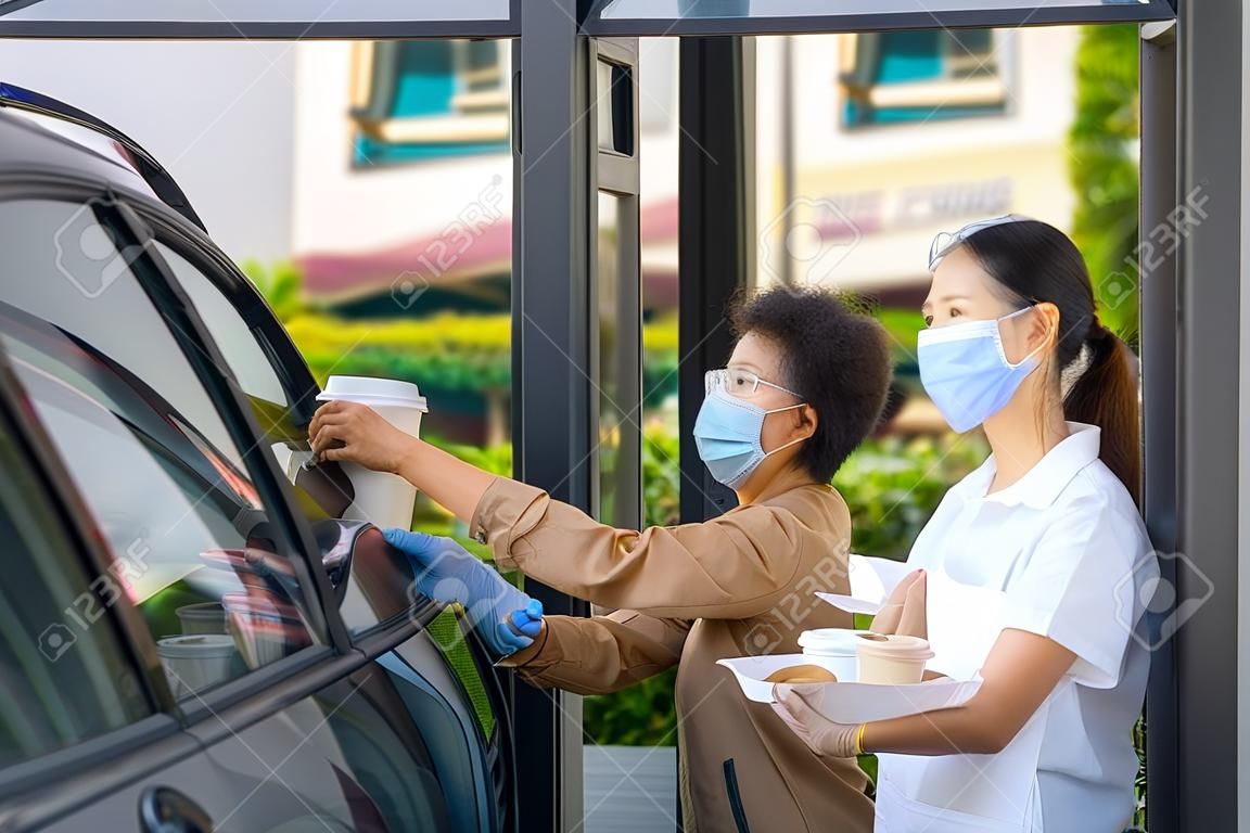 Uomo asiatico in maschera protettiva che prende cibo e caffè con cameriera donna che indossa maschera facciale e schermo facciale durante l'epidemia di coronavirus.