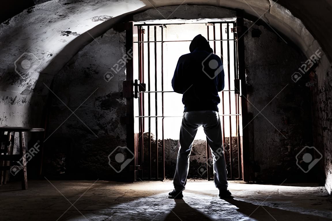 Gefangener Mann eingesperrt im alten unterirdischen Keller stehend, Silhouette von hinten gegen Gitter - Gefangen im dunklen Keller in verzweifeltem Isolationsgefühl - Konzept der Verweigerung der Menschenrechte - Bild