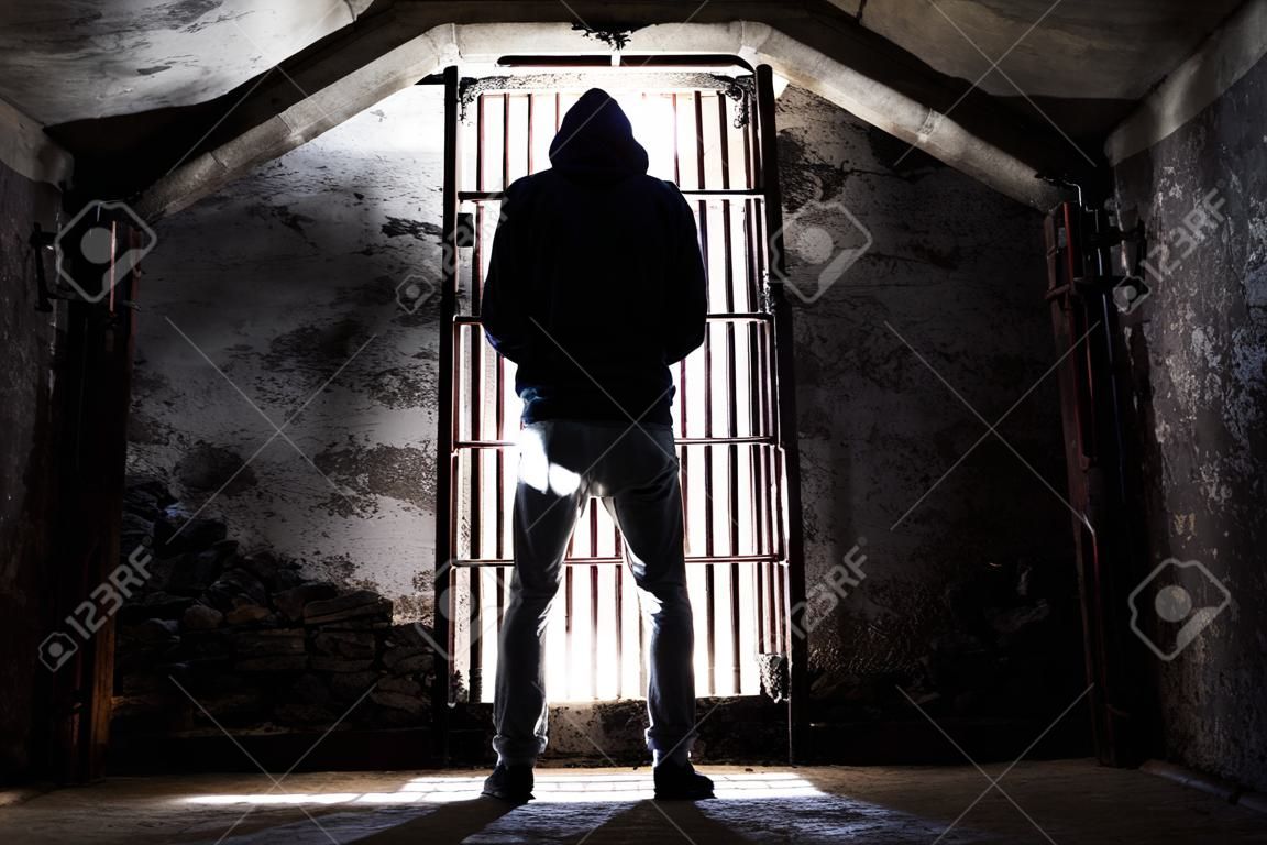 囚人の男は古い地下地下室に立って閉じ込められ、バーに対して後ろからシルエット - 絶望的な孤立感で暗い地下室の中で捕虜 - 否定人権の概念 - 画像