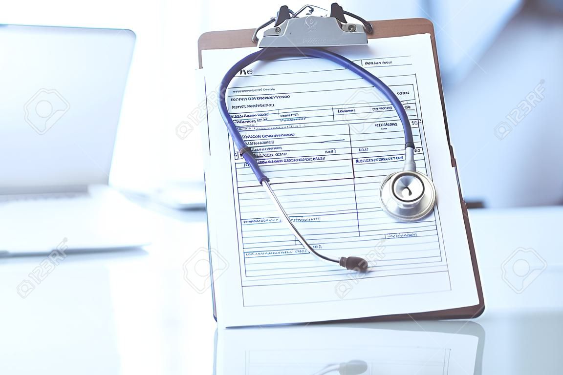 Stethoscope and clipboard with medication history records are on the table at the doctors working place. Medicine and health care concept