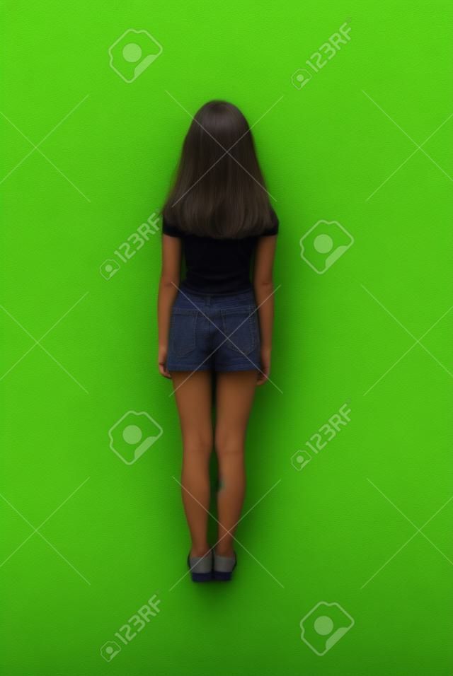 Rear view young girl with long hair looking at wall. Isolated on green background