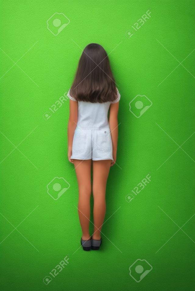 Rear view young girl with long hair looking at wall. Isolated on green background