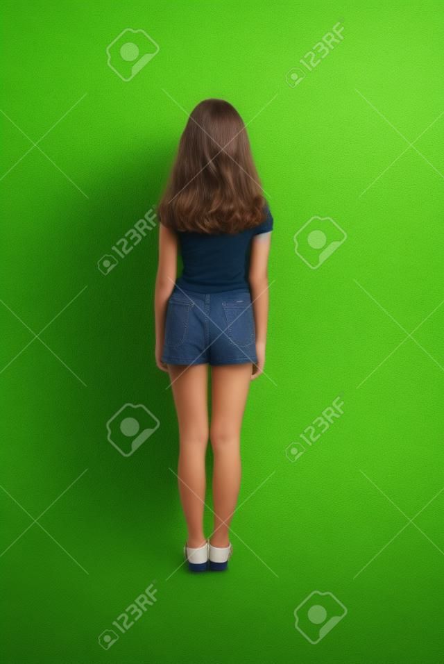 有看牆壁的長的頭髮的背面圖女孩。在綠色背景上孤立