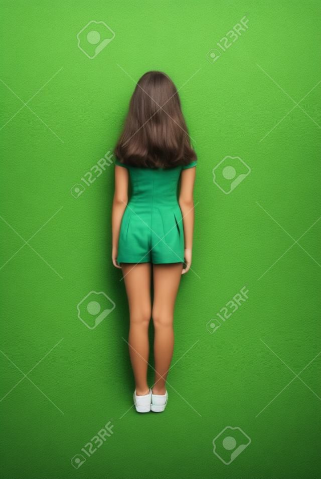 有看牆壁的長的頭髮的背面圖女孩。在綠色背景上孤立