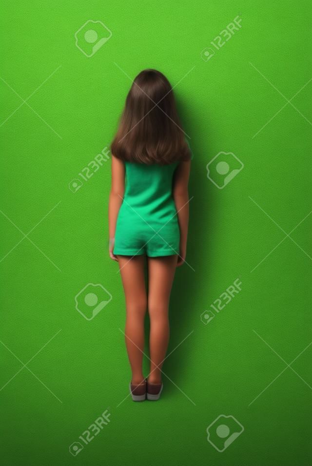Маленькая девочка вид сзади с длинными волосами, глядя на стену. Изолированные на зеленом фоне