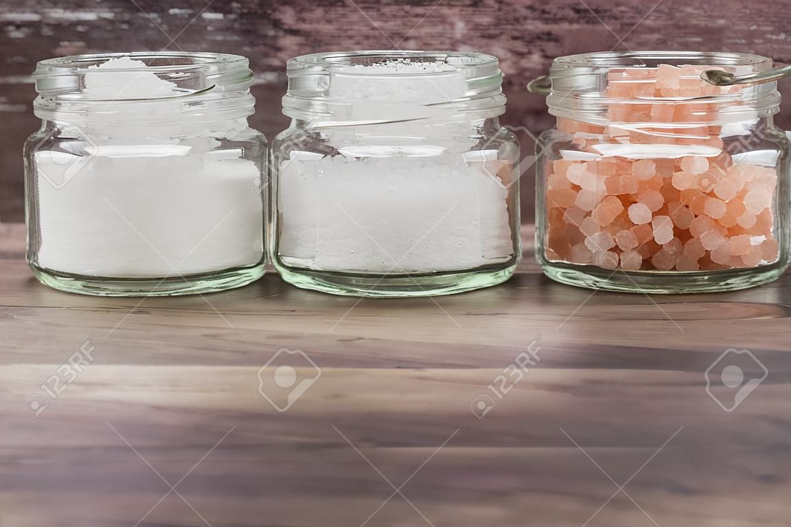 Table salt, sea salt and himalayan salt in mason jar over wooden background