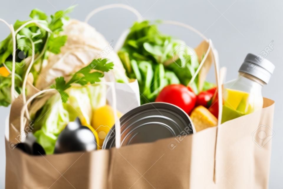 Food in a paper bag. Food donation or food delivery concept. Free space for text. Oil, bread, cabbage, salad, vegetables, canned food. Light gray background, close up