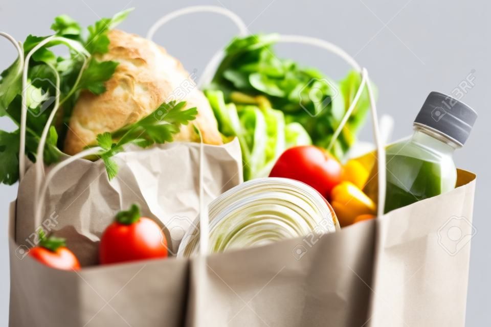 Comida en una bolsa de papel. Donación de alimentos o concepto de entrega de alimentos. Espacio libre para texto. Aceite, pan, repollo, ensalada, verduras, conservas. Fondo gris claro, de cerca