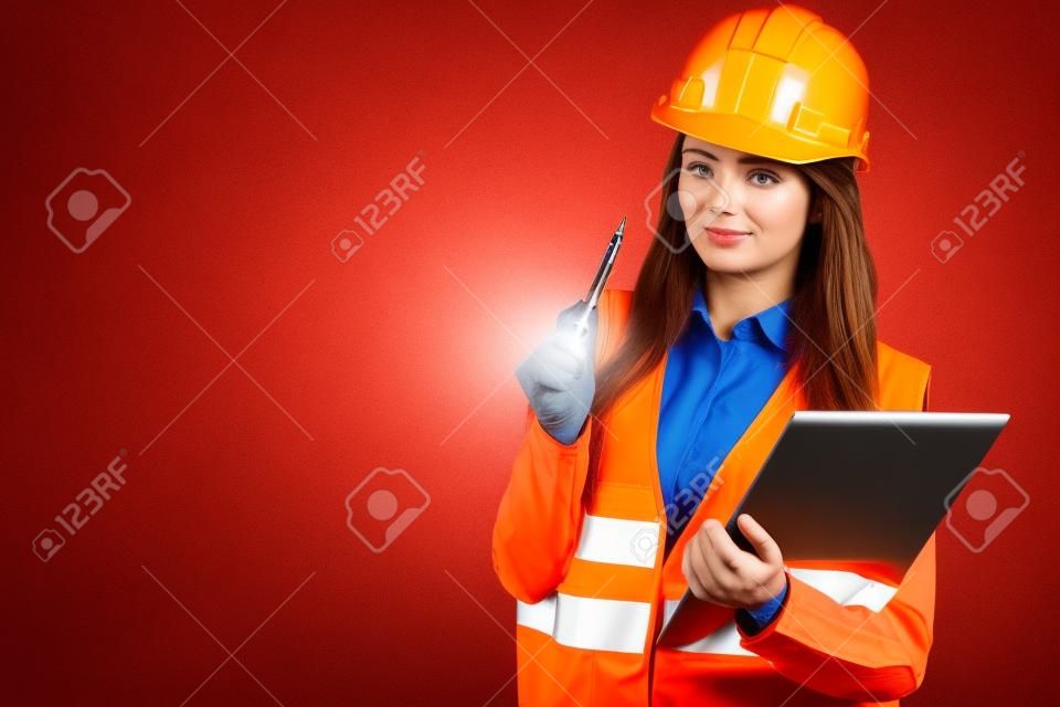 Woman construction worker builder structural engineerin in orange vest red hard helmet holds pen file pad. Safety in industrial work. Studio shot
