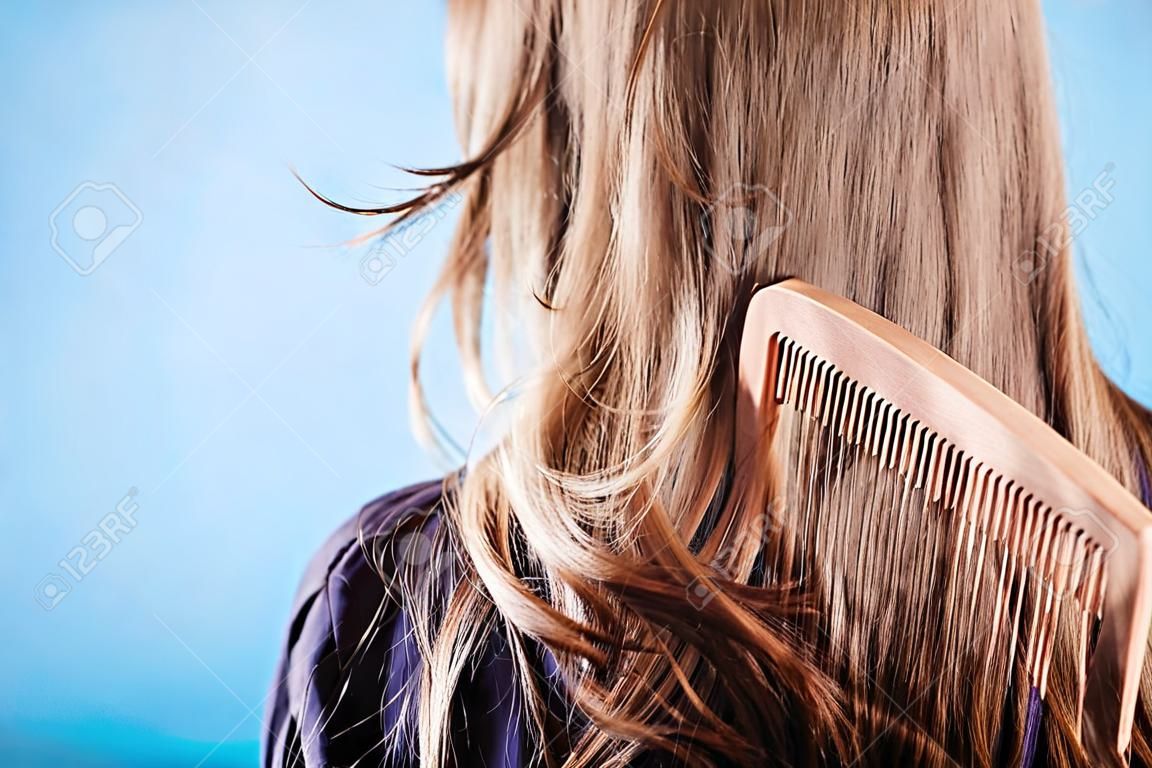 Haircare concept. Straight brown hair with wooden comb closeup
