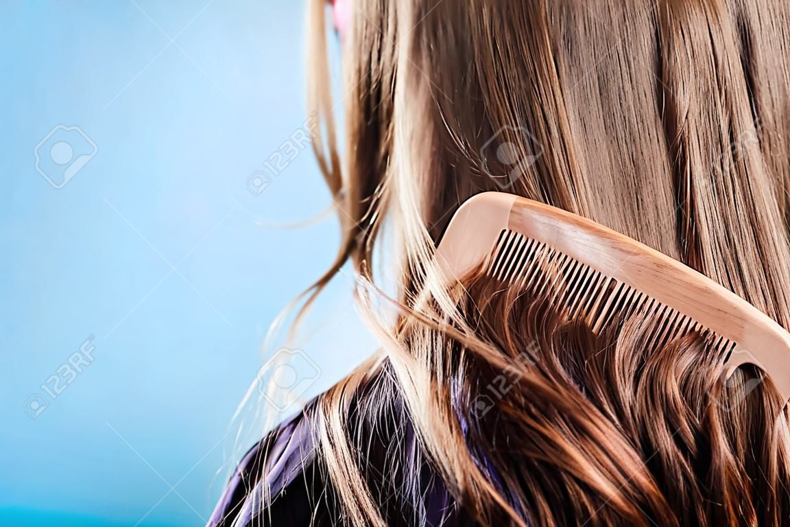 Haircare concept. Straight brown hair with wooden comb closeup