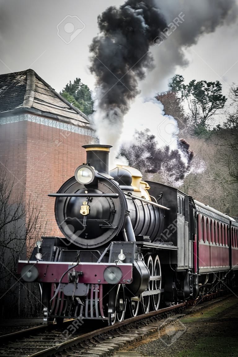 A upright vertical view of a steam train locomotive in motion facing forward and smoking