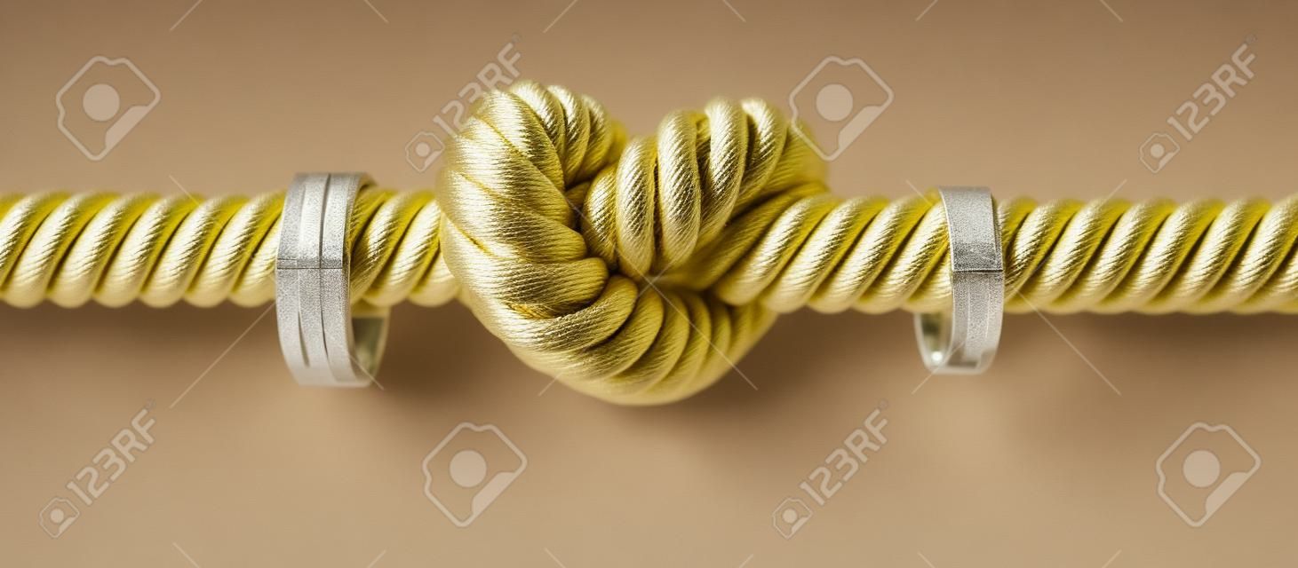 Une corde grossière avec un noeud lié au milieu enfilé à travers deux anneaux de mariage attachées de chaque côté sur un fond isolé