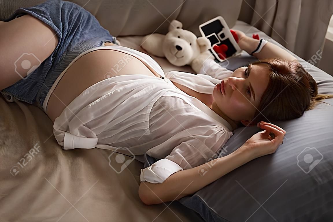 Junge schöne schwangere Frau liegt auf dem Bett im Schlafzimmer