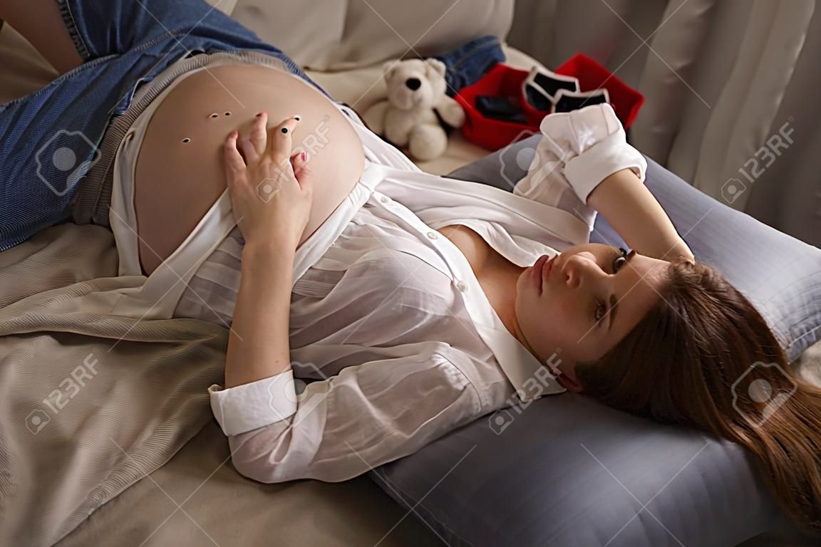 Junge schöne schwangere Frau liegt auf dem Bett im Schlafzimmer