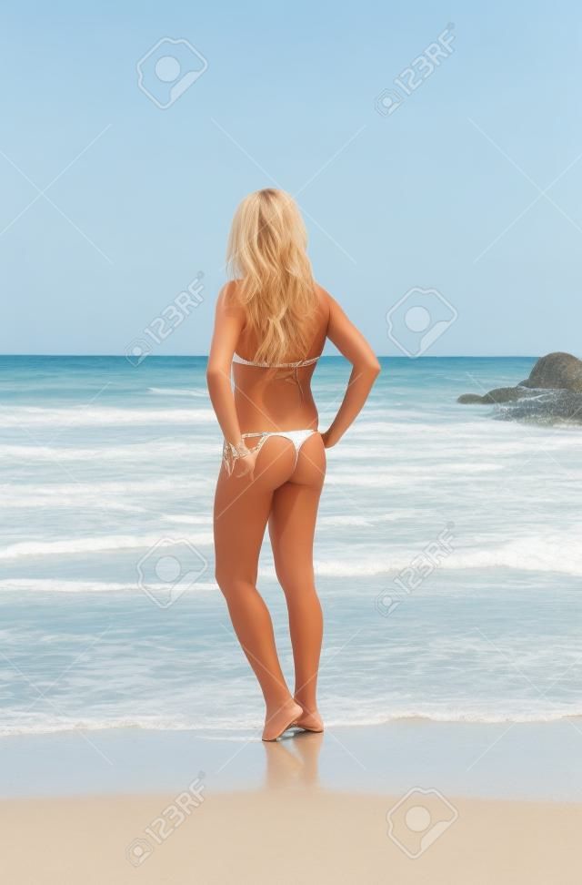 Hermosa rubia delgada en la playa. Vista posterior de la