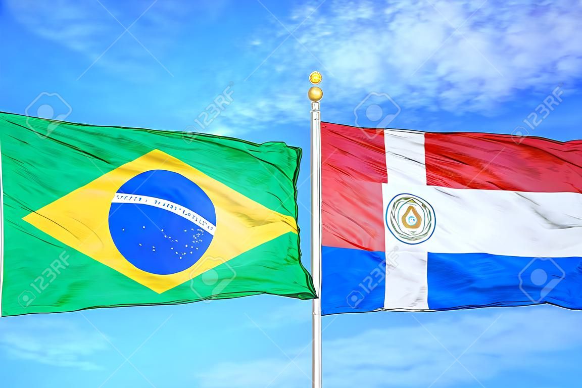 Brazil and Paraguay two flags on flagpoles and blue cloudy sky background