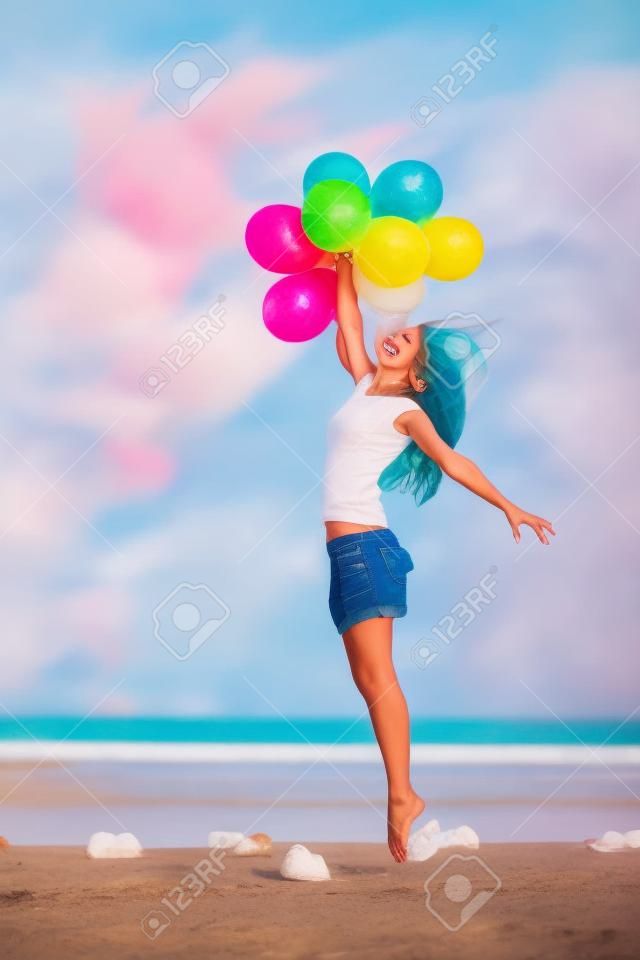 Boldog lány, aki csokor színes hőlégballonok a strandon