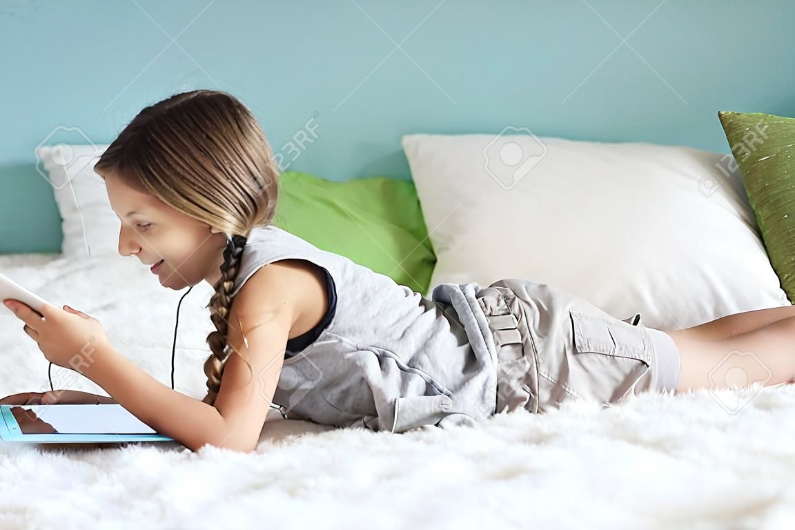 Предварительно подросток расслабляется в постели и слушать музыку с наушниками на планшете дома