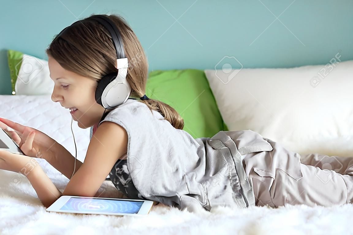Предварительно подросток расслабляется в постели и слушать музыку с наушниками на планшете дома