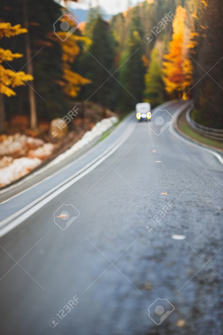 Autumn road among forest to the mountains. Fall travel, bad weather. Out of focus.