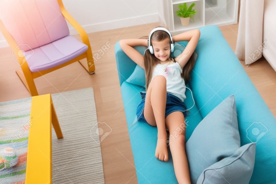 10 ans entre fille de détente sur un canapé, écouter de la musique dans les écouteurs et jouer avec tablette pc. Enfant refroidissement sur le canapé dans le salon.