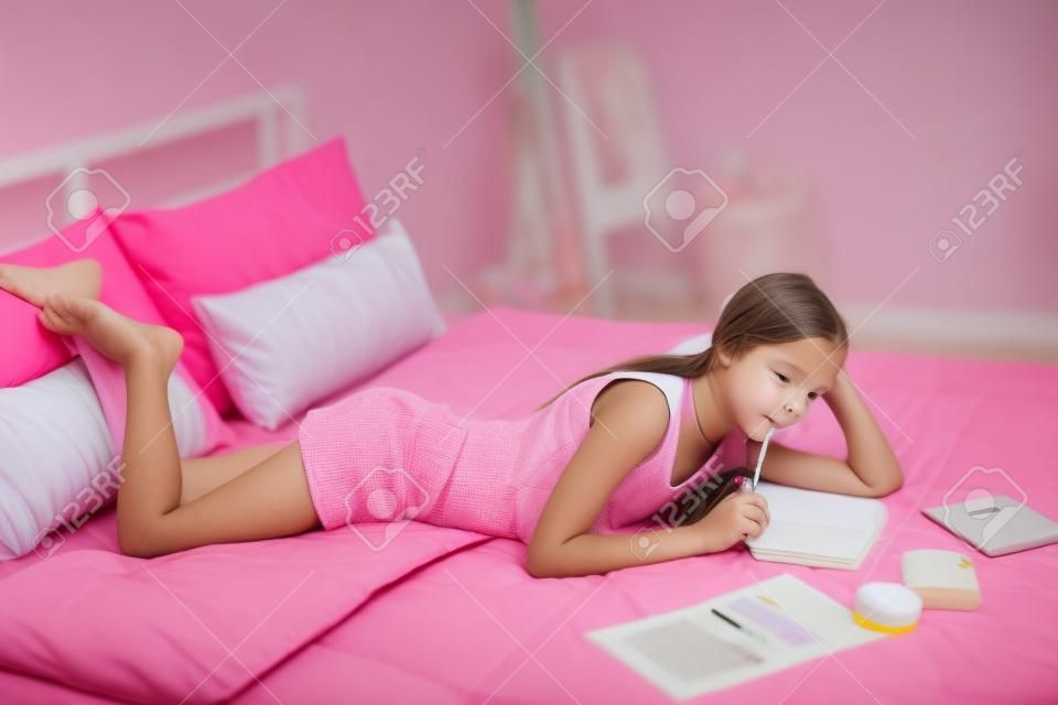 pembe yatak odasında 10-12 yaş öncesi genç kız yapıyor okul ödevi