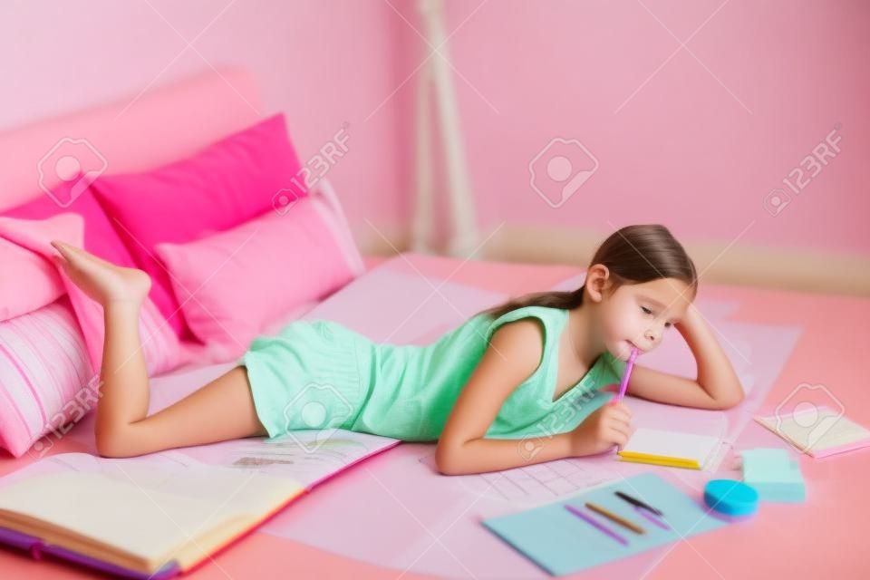 pembe yatak odasında 10-12 yaş öncesi genç kız yapıyor okul ödevi
