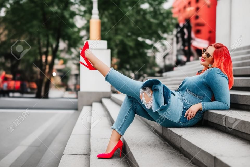 Preriry穿著明亮的五顏六色的夾克的年輕女子，撕開牛仔褲和腳跟鞋走在城市街道上。休閒時尚，加上尺碼模特兒。