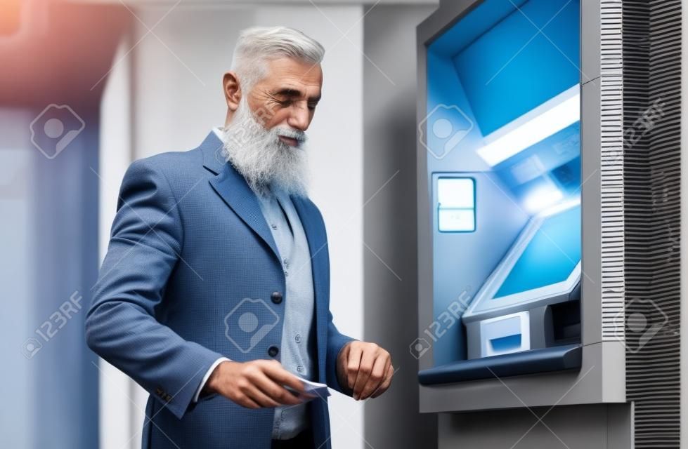 Senior man withdraw money from bank cash machine with debit card - Bearded hipster mature male doing payment with credit card in ATM - Concept of business, banking account and elderly lifestyle people