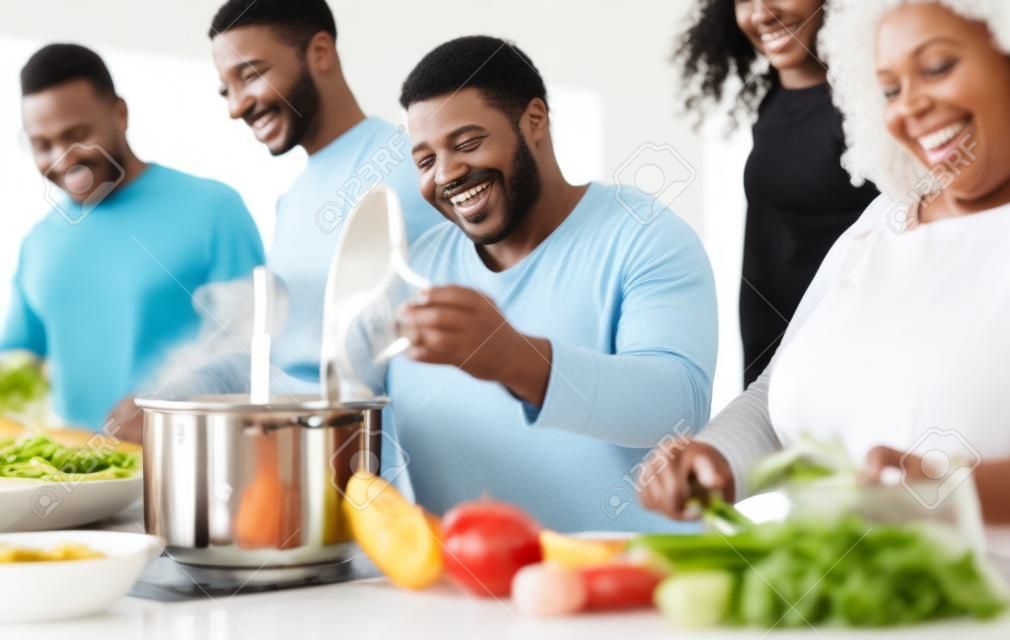 モダンなキッチンで一緒に料理を楽しんでいる幸せな黒人家族-食べ物と両親の団結の概念